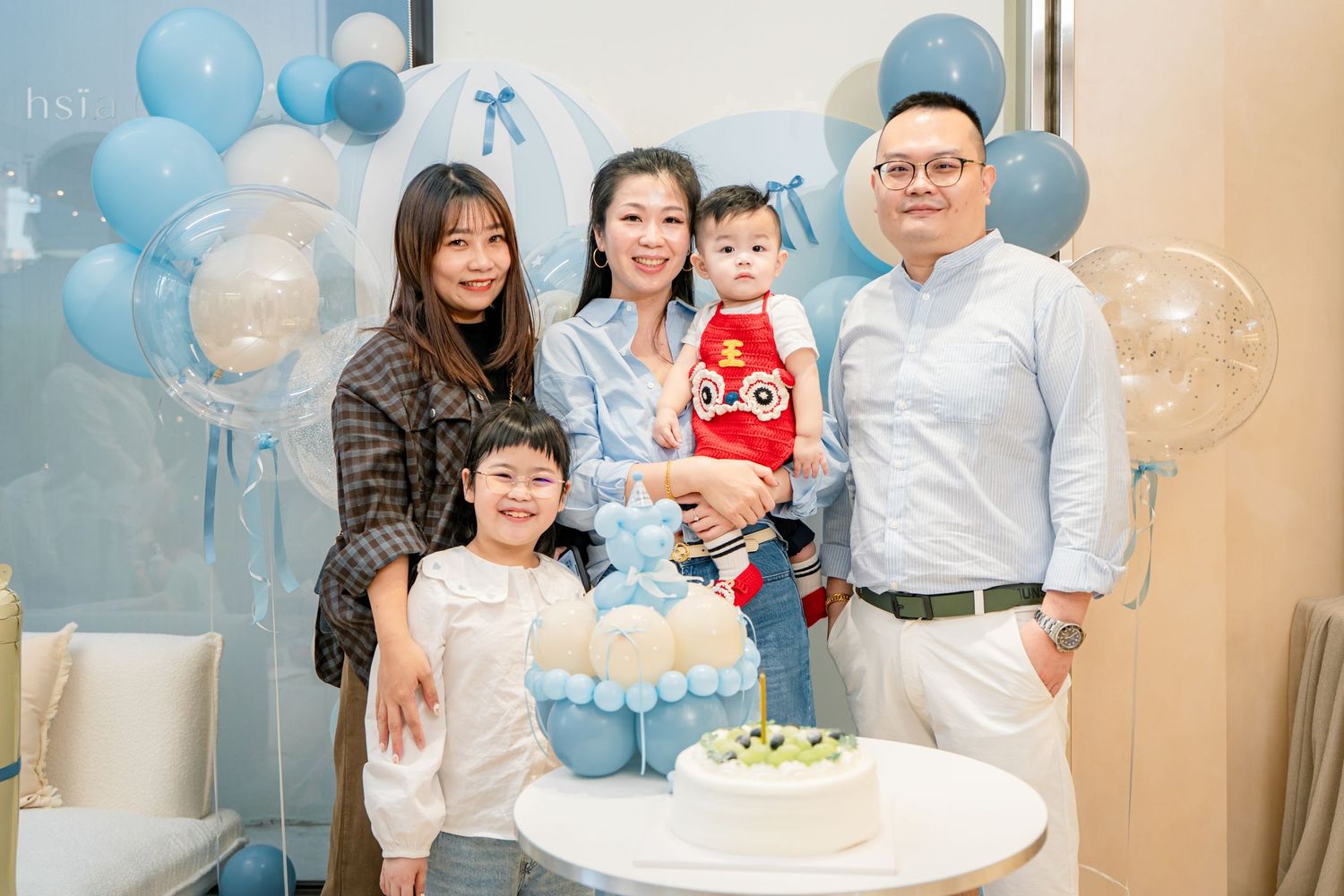 A baby shower celebration decorated with blue balloons featuring a white cake and guests gathering around a table.