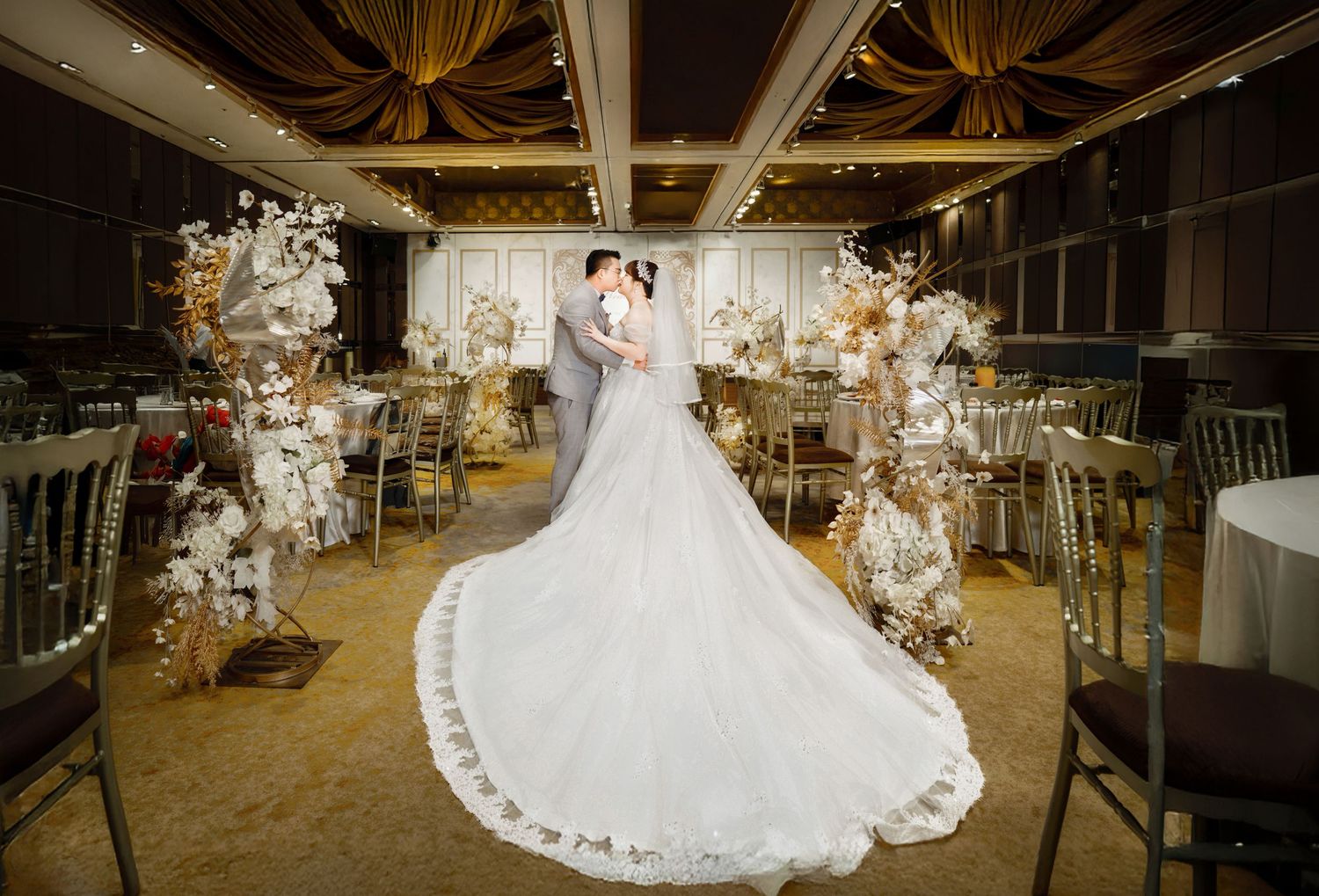 A romantic wedding couple dances together in an elegantly decorated rustic barn venue with warm lighting and floral decor.