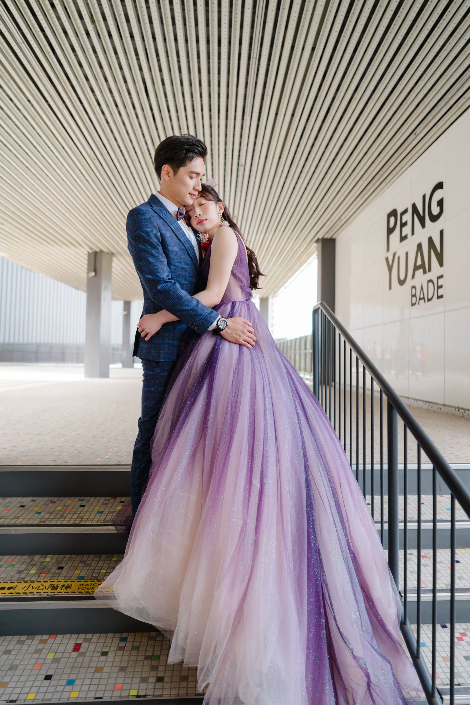 A couple embraces in a stairwell with bride wearing an ombre purple ballgown and groom in navy suit.