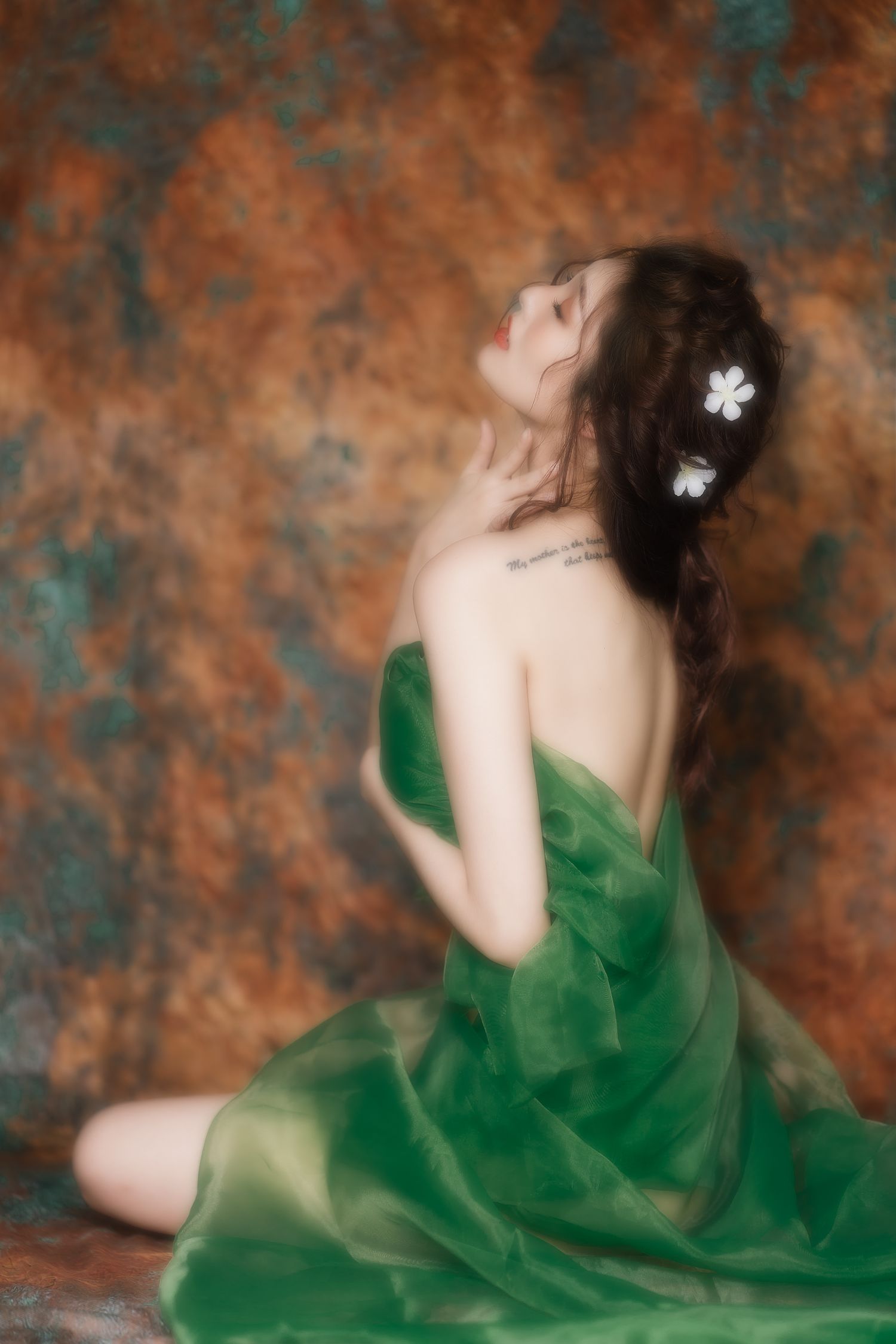 Artistic portrait with soft focus of person in flowing emerald green dress against textured rust and teal background.