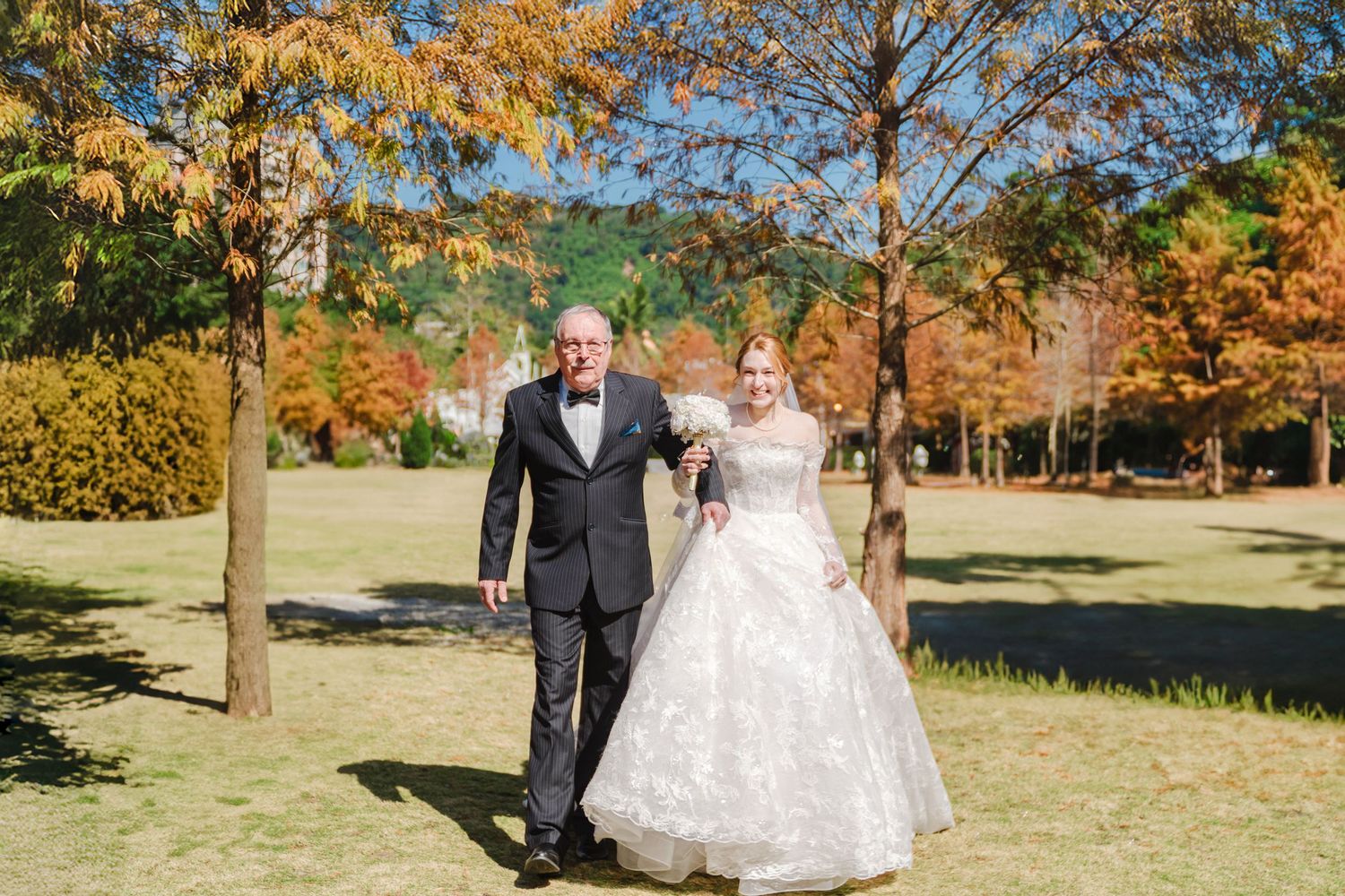 A couple walks hand in hand through a sunny autumn park with golden foliage and beautiful fall colors in the background.