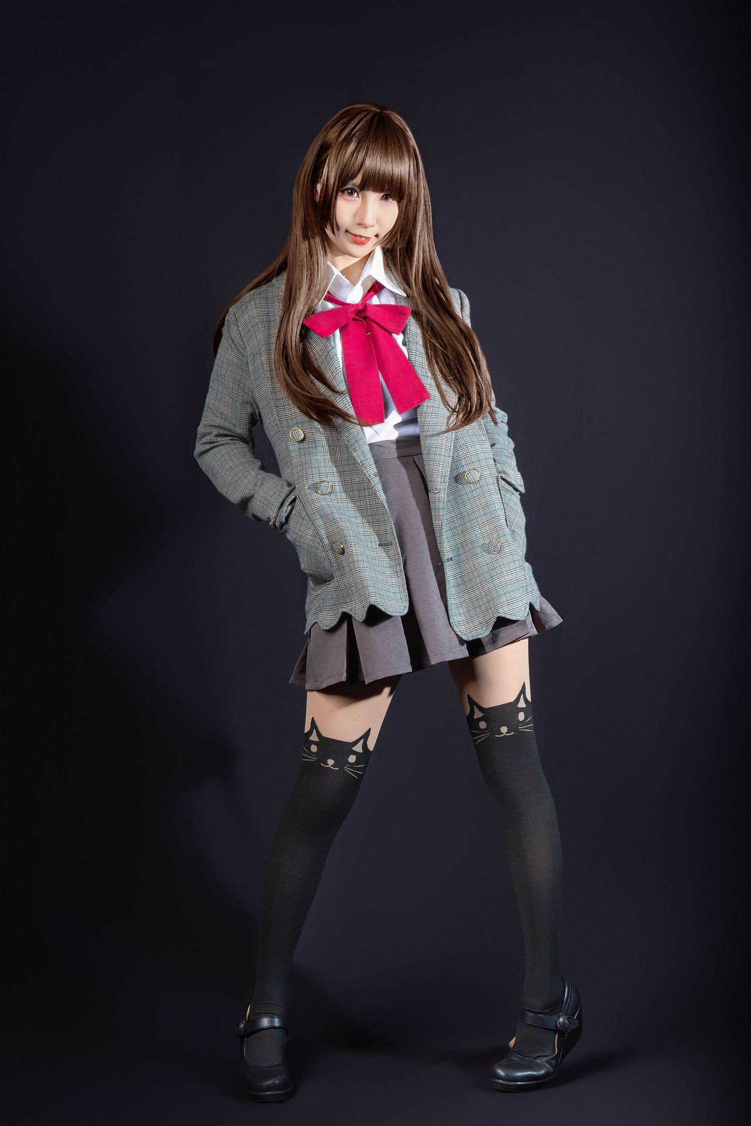Person wearing school uniform style outfit with gray blazer, red bow tie, pleated skirt and knee-high socks against dark background.