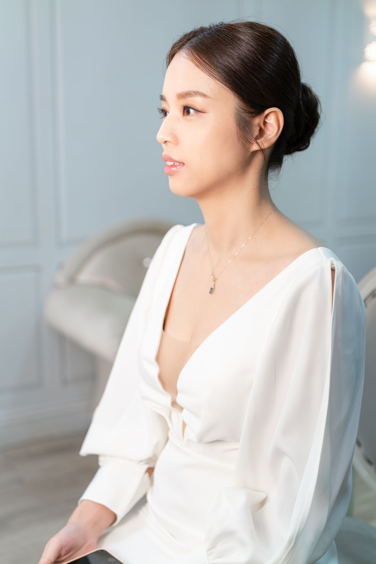 A person in an elegant white dress with long sleeves and a plunging neckline sits gracefully against a light background.