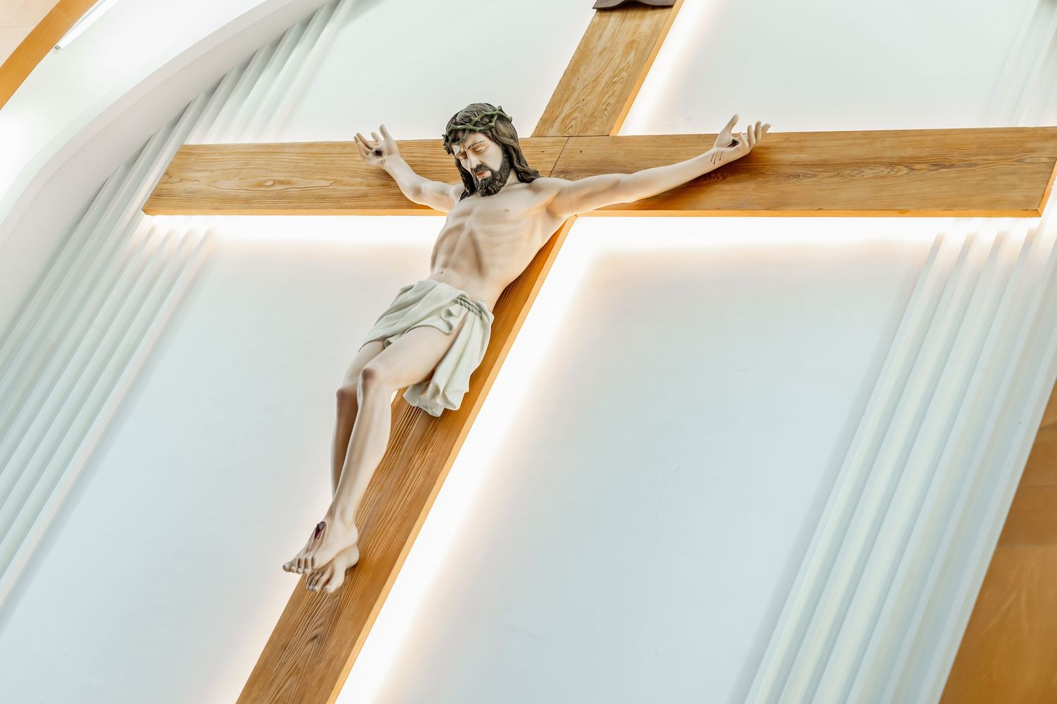 A crucifix mounted on a white wall displays a wooden sculpture of Jesus.