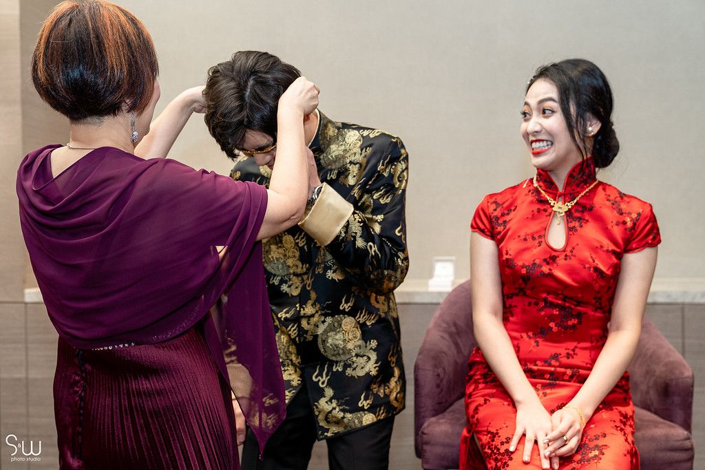 A bride in a red qipao dress gets her hair styled during wedding preparations.