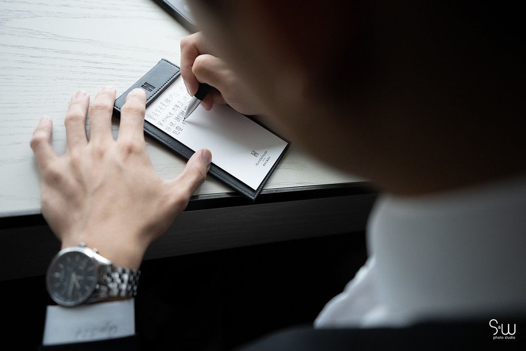 Close-up shot of hands writing on paper while wearing a formal suit and watch.