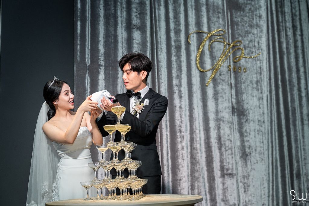 Wedding couple pours champagne into tower of glasses during reception celebration.