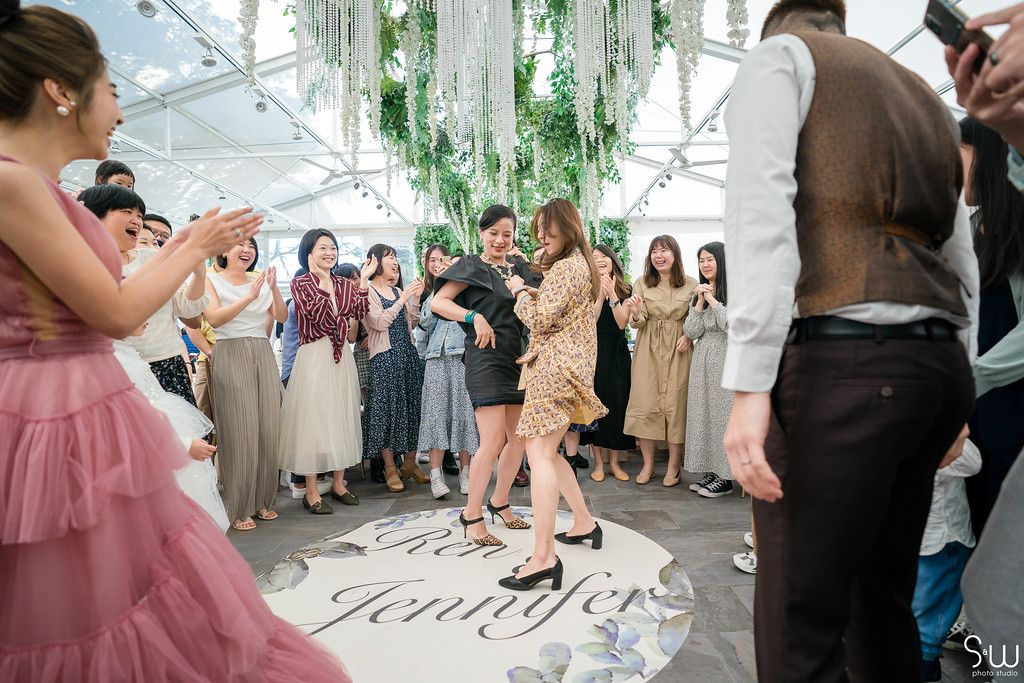 Party guests dancing and celebrating on a decorated dance floor under draped greenery and lights.