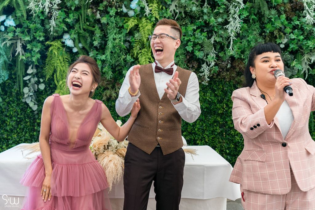 Three attendees sharing a joyful moment of laughter against a wall of greenery.