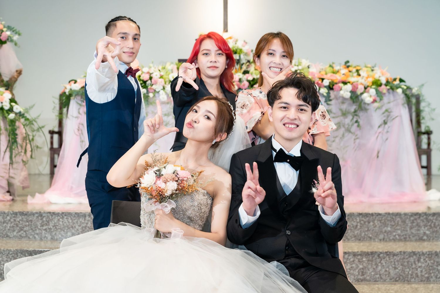 Wedding party makes peace signs while posing for fun photo with floral decorations.
