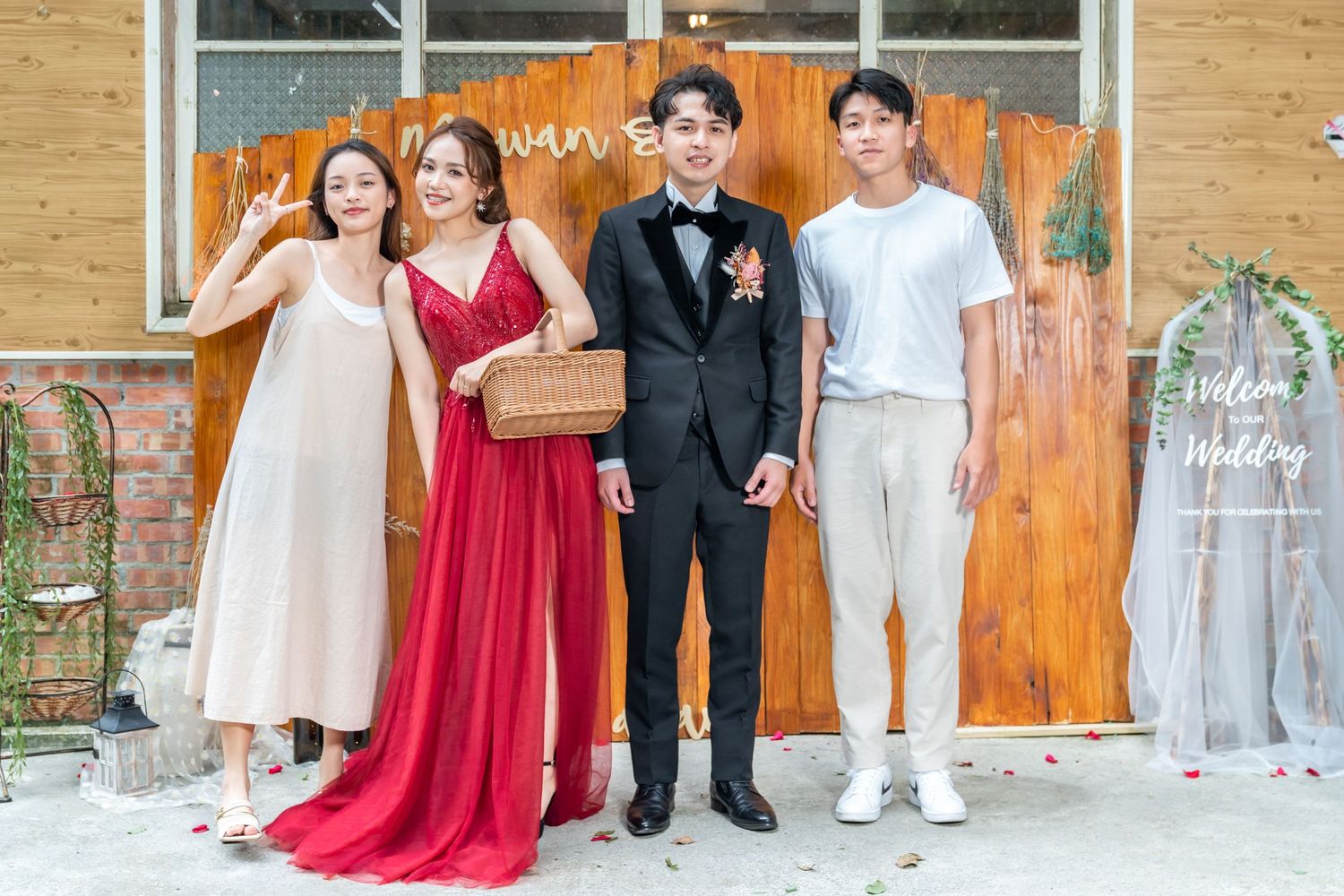 Four people in formal attire pose against rustic wooden wall with decorative elements.