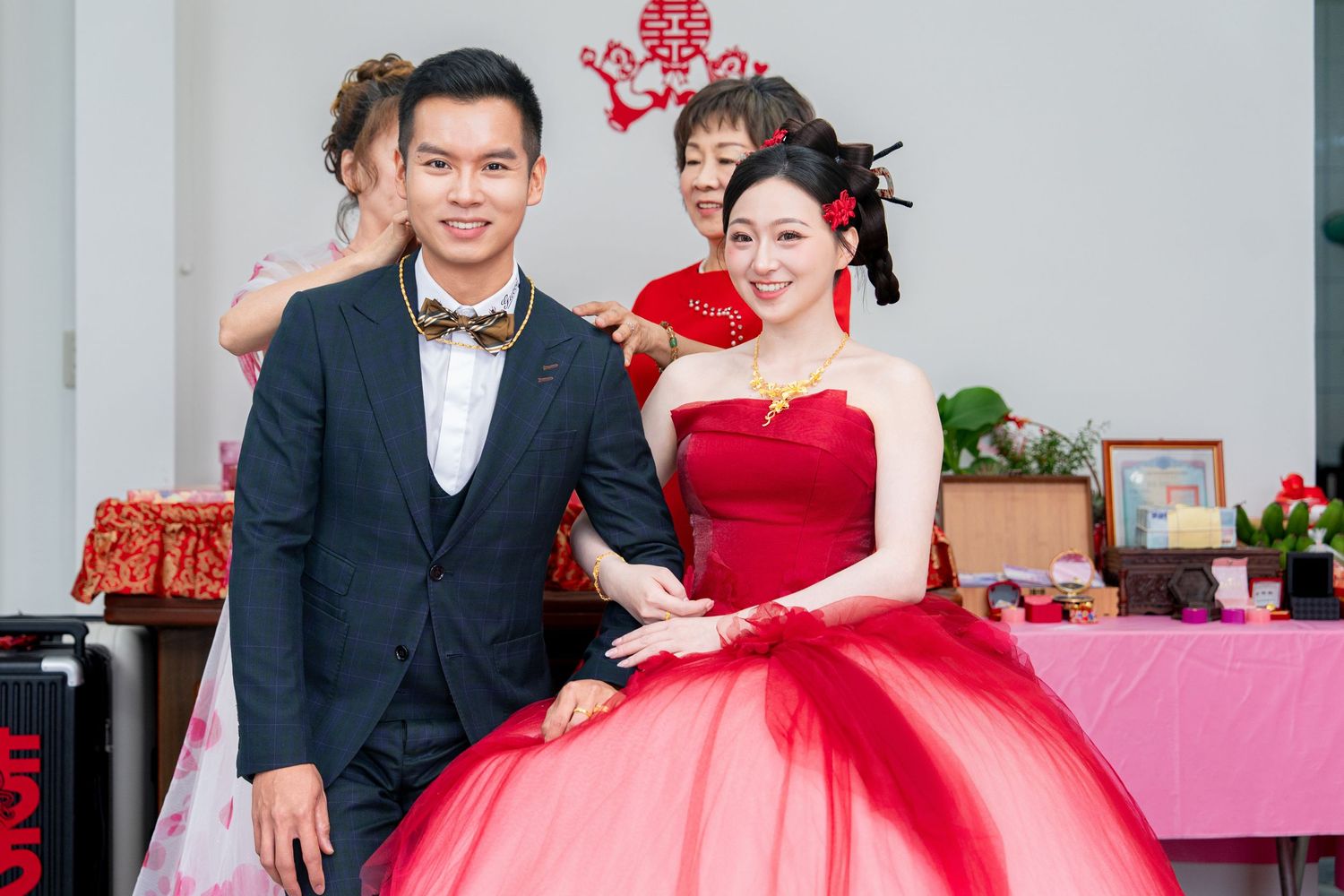 Couple in traditional Chinese wedding attire, groom in navy suit and bride in red ballgown, posing at a festive ceremony.
