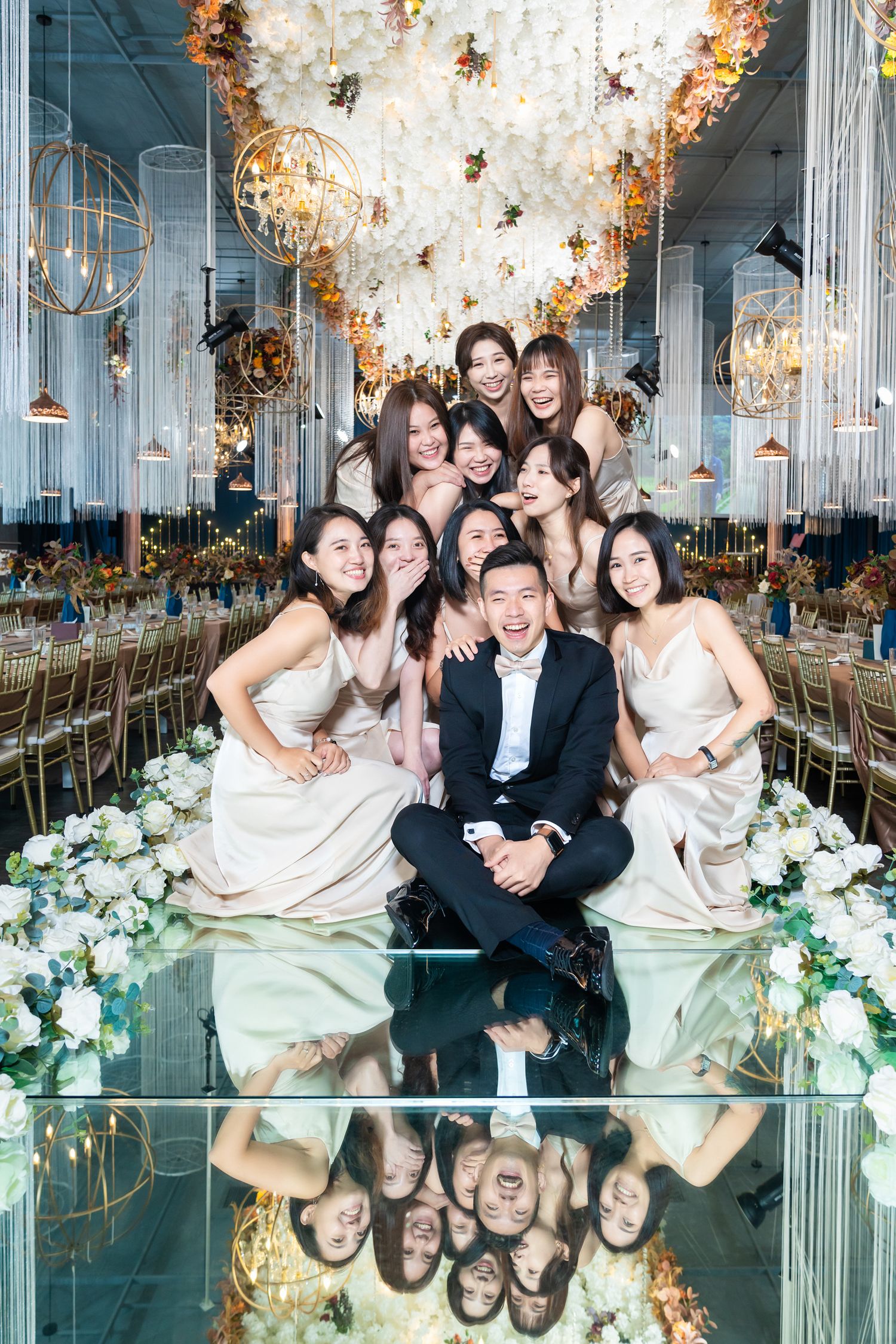 Elegant wedding reception setup with floral decor, mirrored floors and ornate gold chandeliers in a luxurious ballroom.
