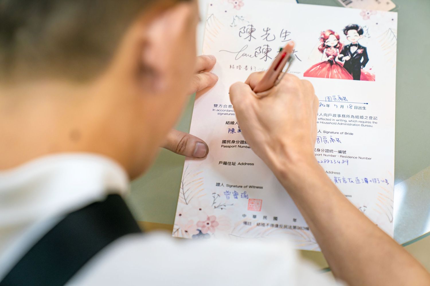 Person writing on a white paper with pen while sitting at a desk in a well-lit room.