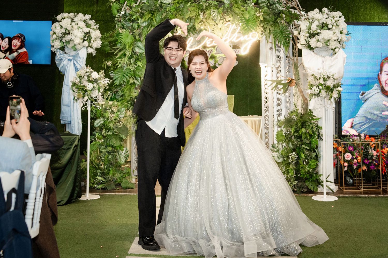 Elegant wedding couple dancing and celebrating with guests under floral decorations at an outdoor garden reception.