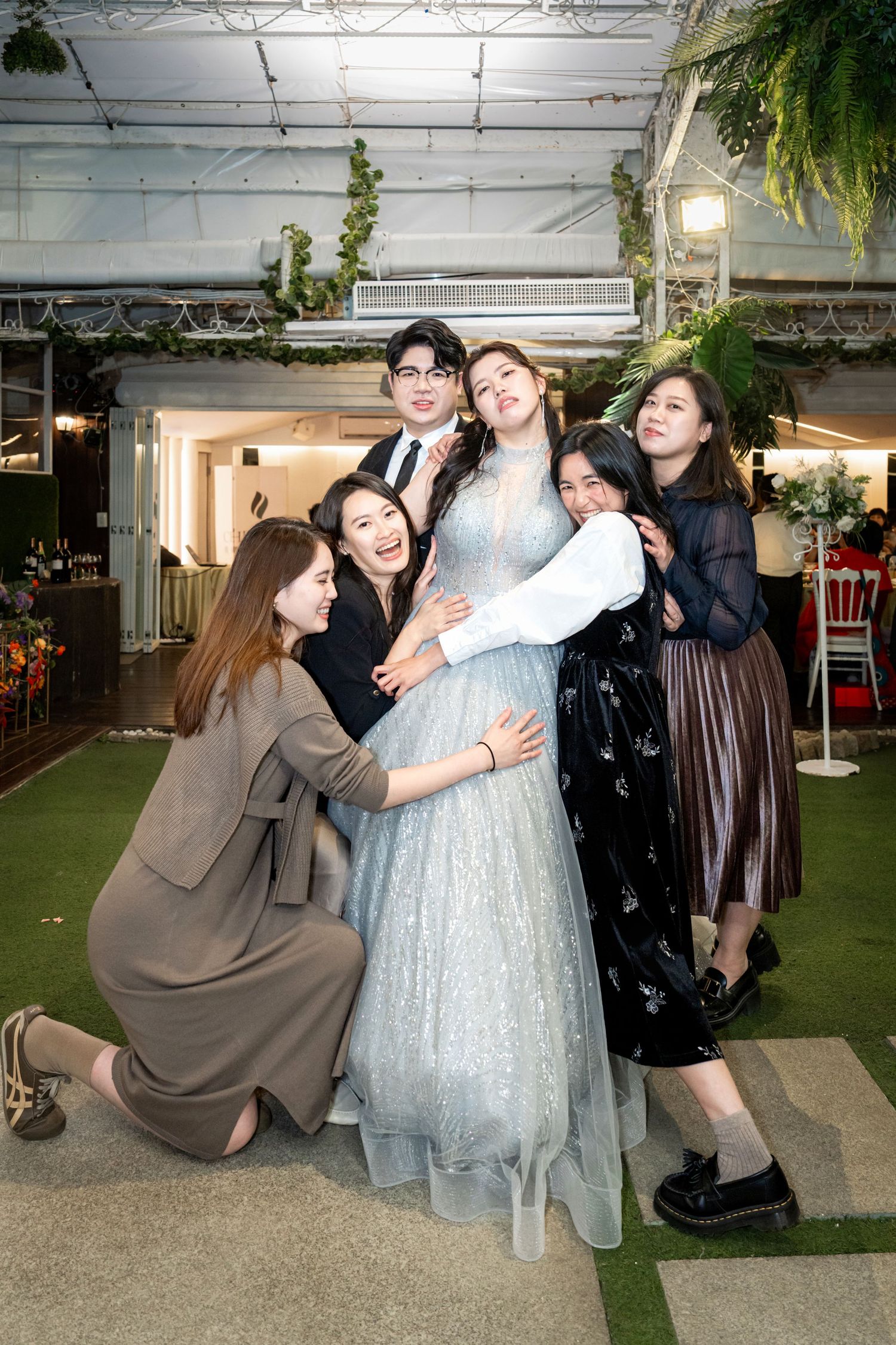 A group of friends pose together at an indoor venue with a person in a sparkly light blue gown as the centerpiece.