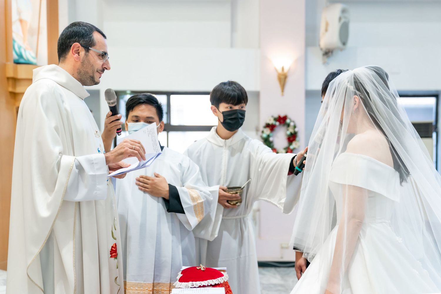 A priest performs a wedding ceremony ritual with altar servers assisting.