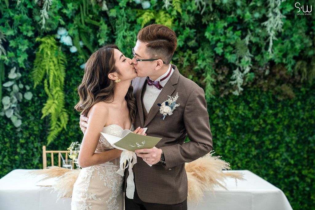 Couple shares an intimate moment during their wedding ceremony against a lush green wall backdrop.