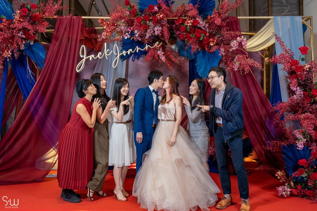 Wedding celebration candid moment with guests on red carpet under floral decorations.