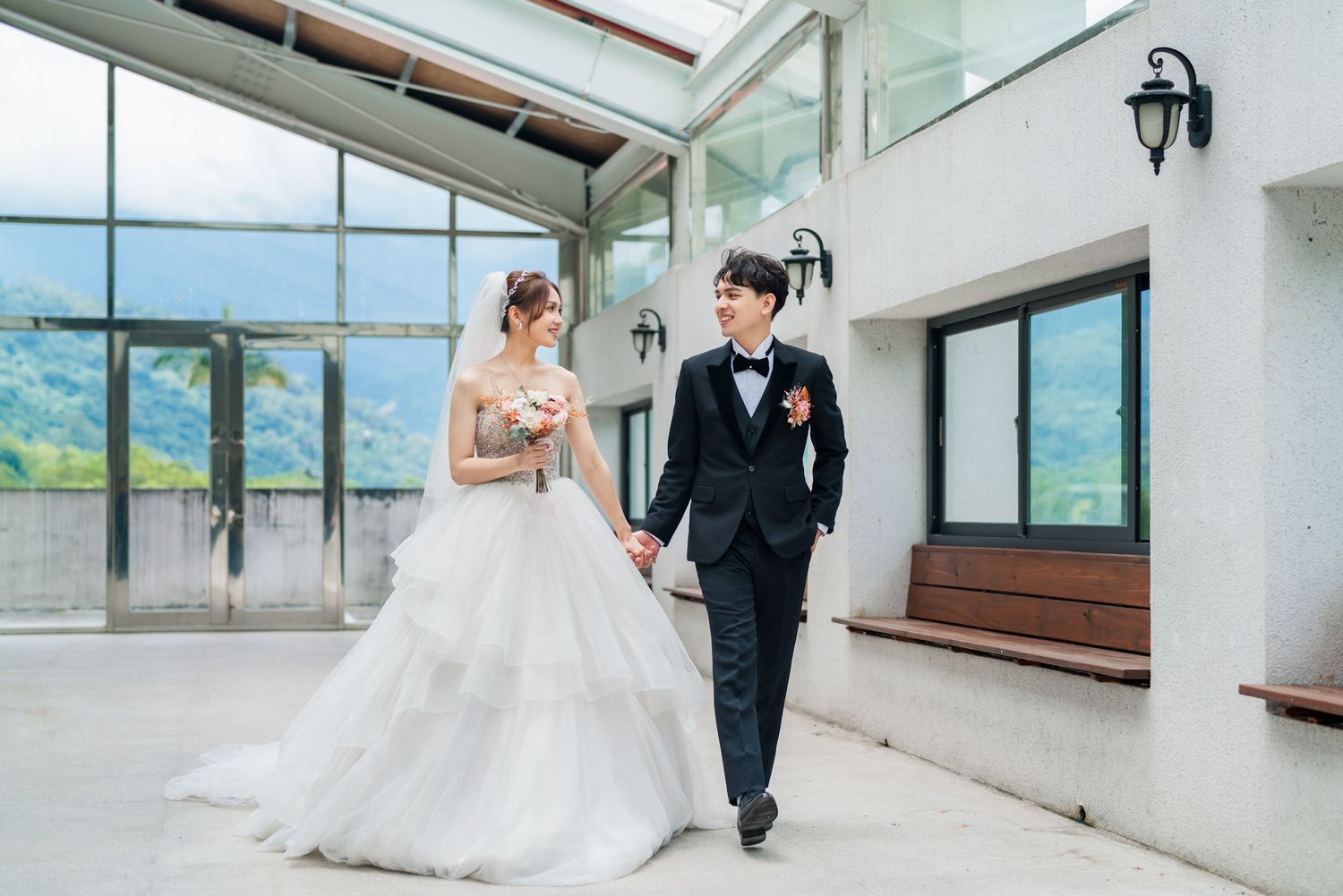 Elegant wedding couple walking together in modern building with mountain views.