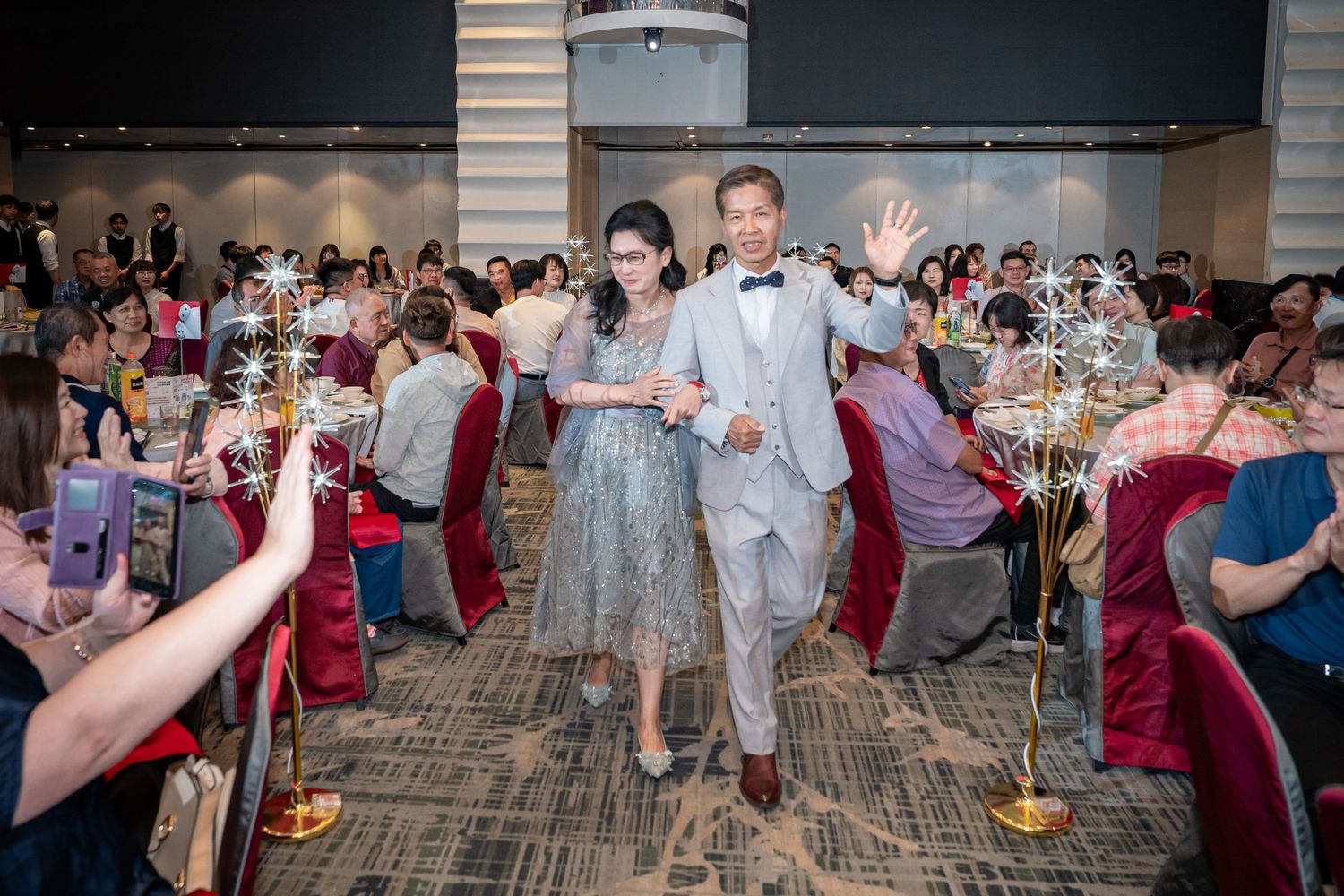 Elegant couple walks through banquet hall at wedding reception, surrounded by guests and decorative star centerpieces.