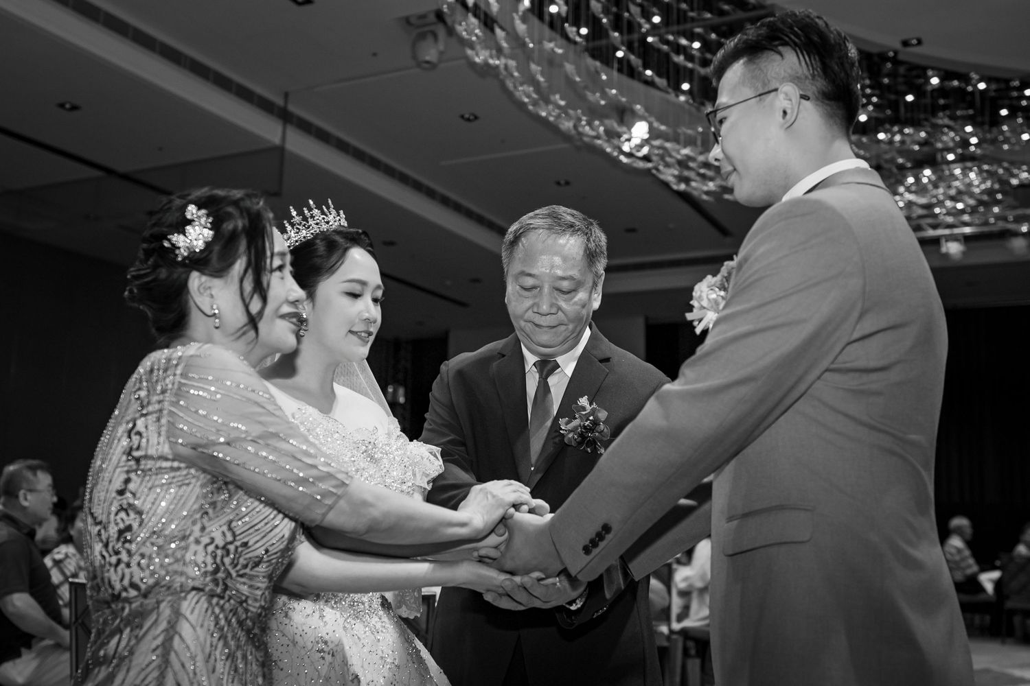 Group of wedding guests enthusiastically dancing together at a reception under crystal chandeliers.