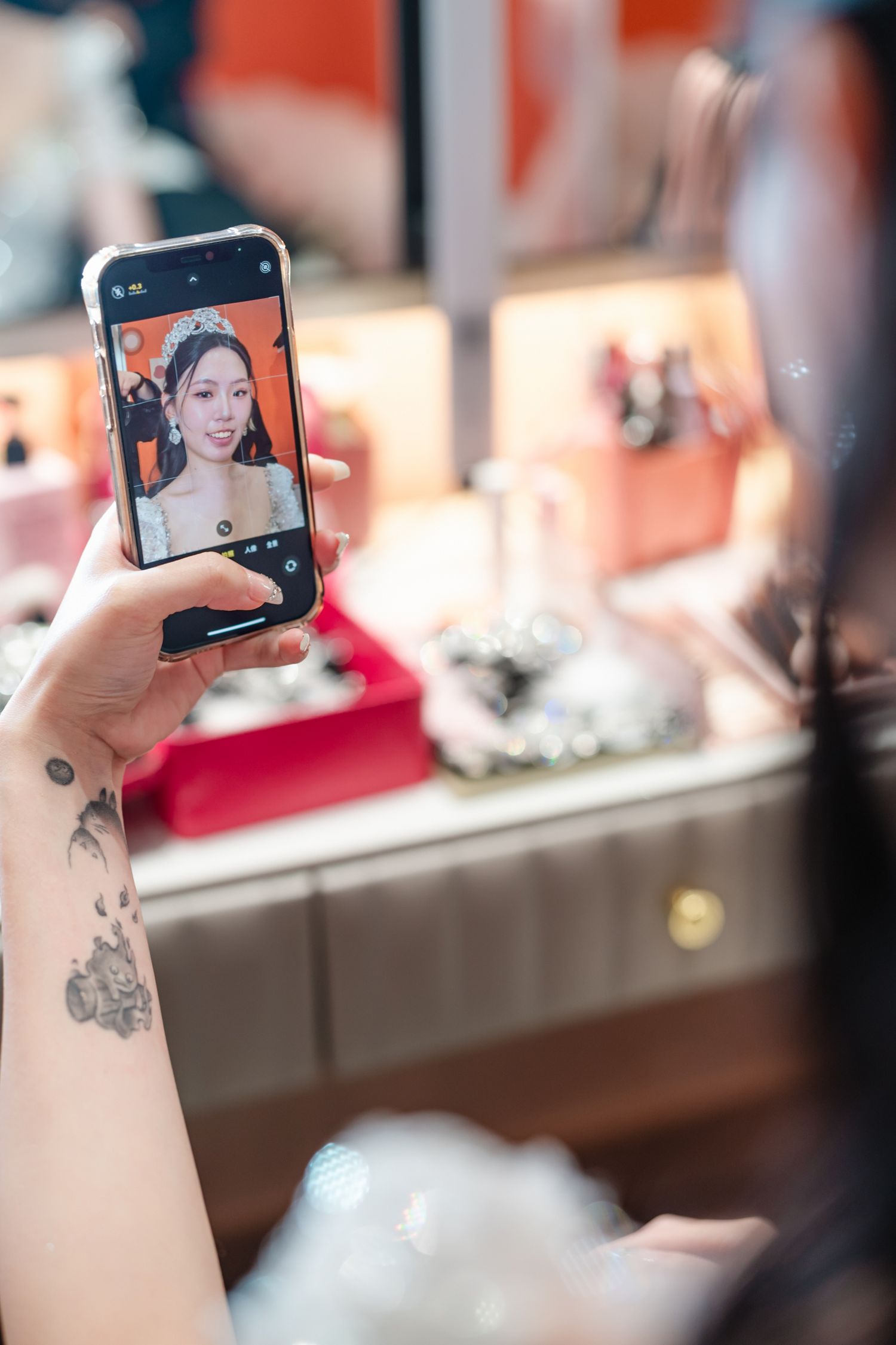 Tattooed hand holding smartphone taking selfie photo with display screen visible in reflective mirror.