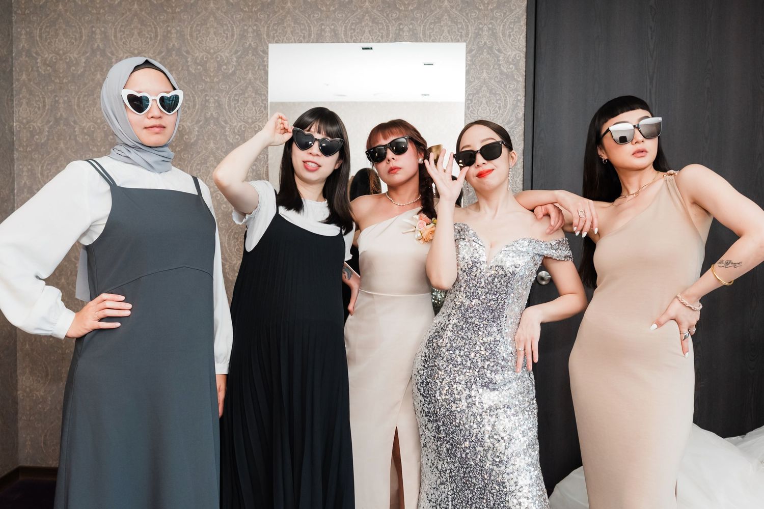 Five friends pose together at a formal event wearing elegant dresses in neutral tones and sunglasses.