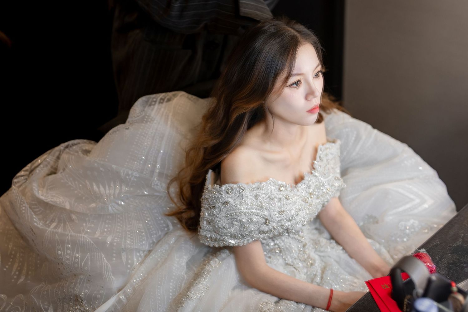 A person in an elegant white lace wedding dress poses gracefully in a dimly lit setting.