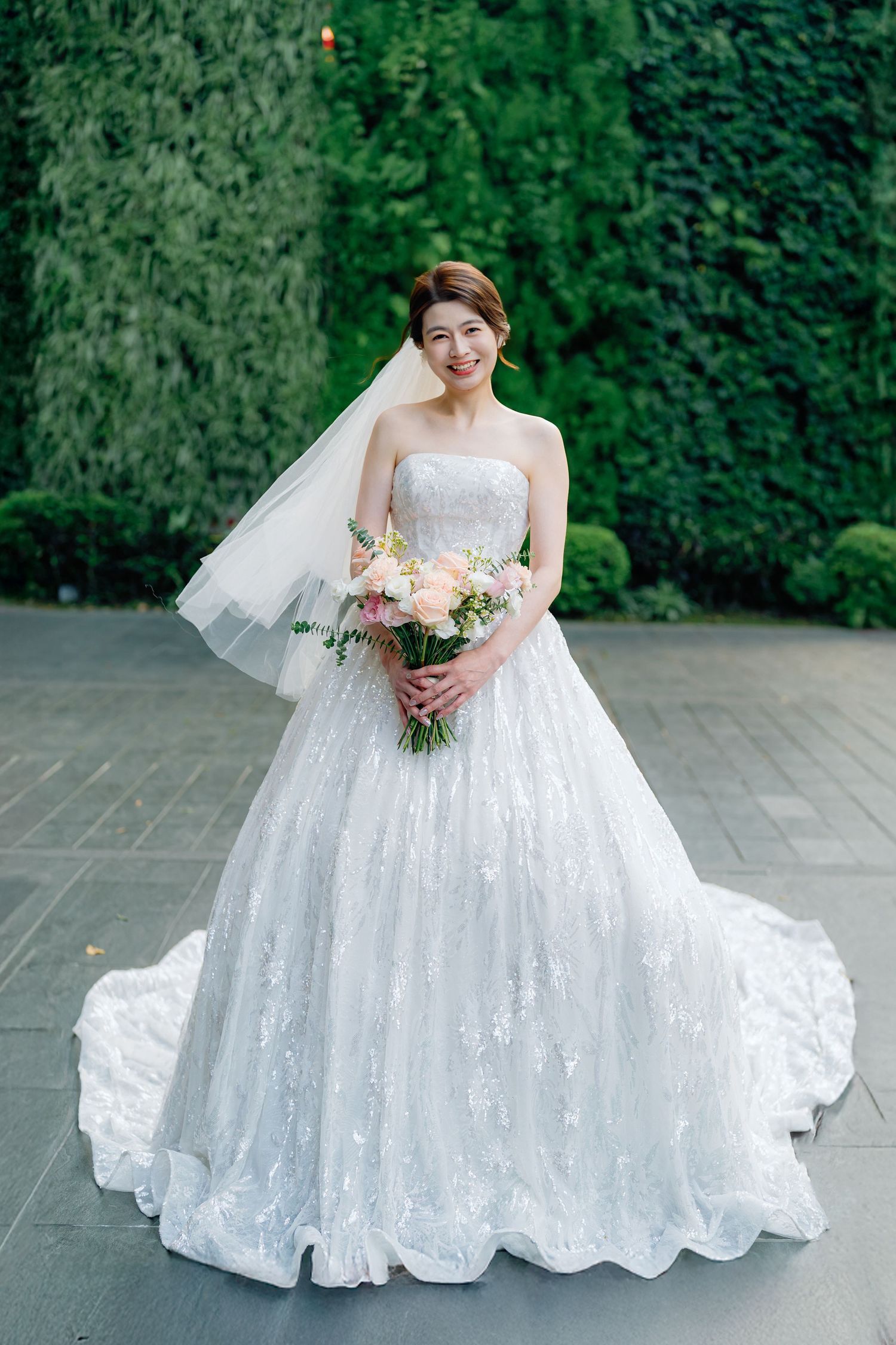 A wedding dress with lace details billows out on a stone patio surrounded by lush greenery in a photo series.