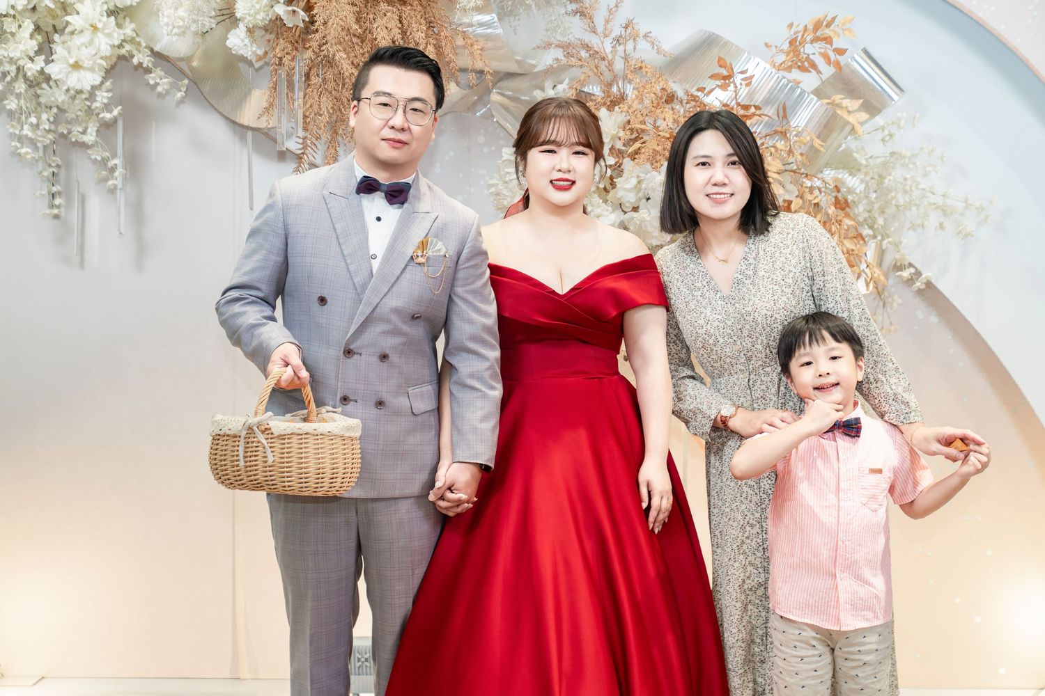 A group poses together in formal attire featuring red dresses and gray suits against a neutral studio backdrop.