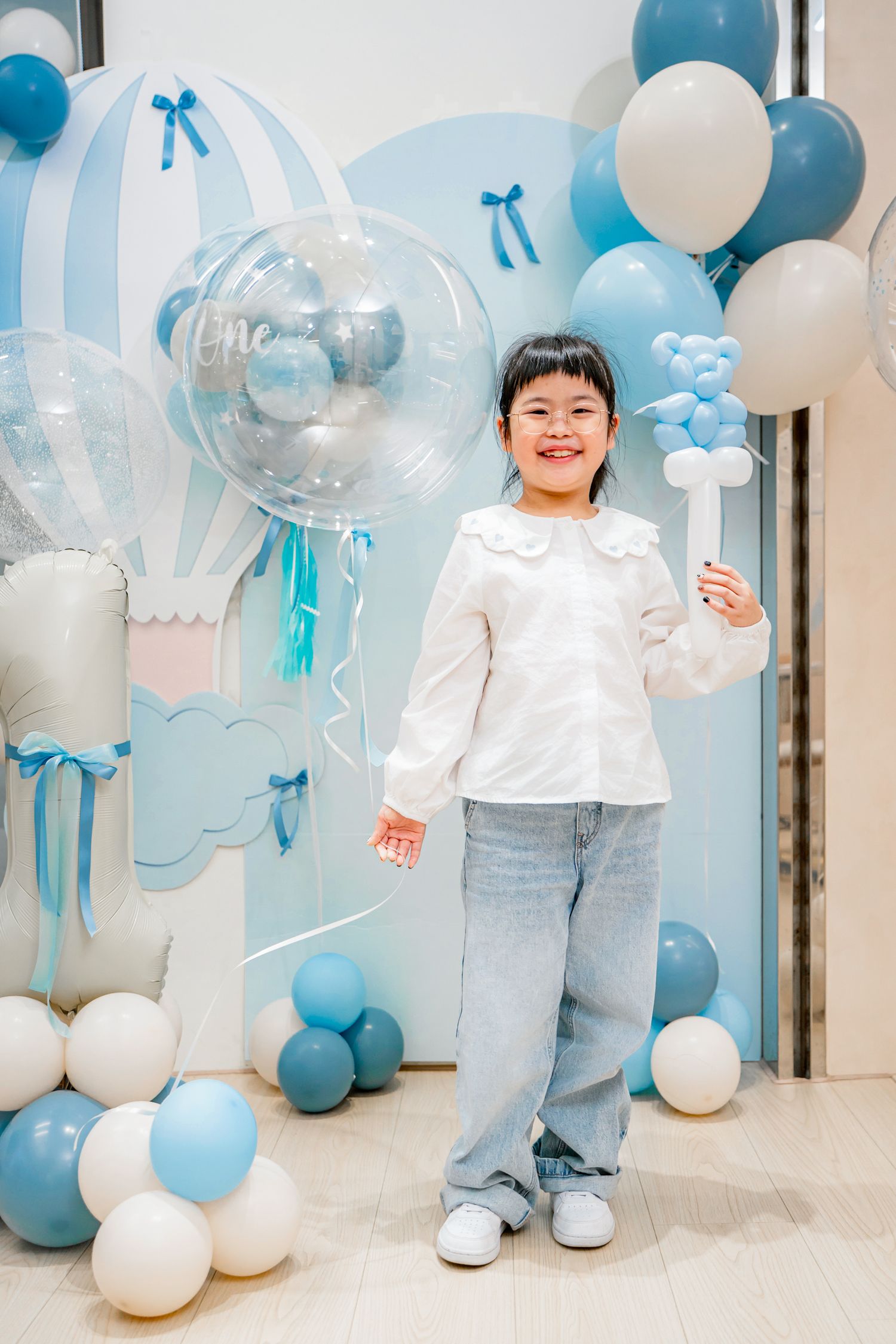 Blue and white balloon decorations create a festive atmosphere for a child's celebration against a white wall.