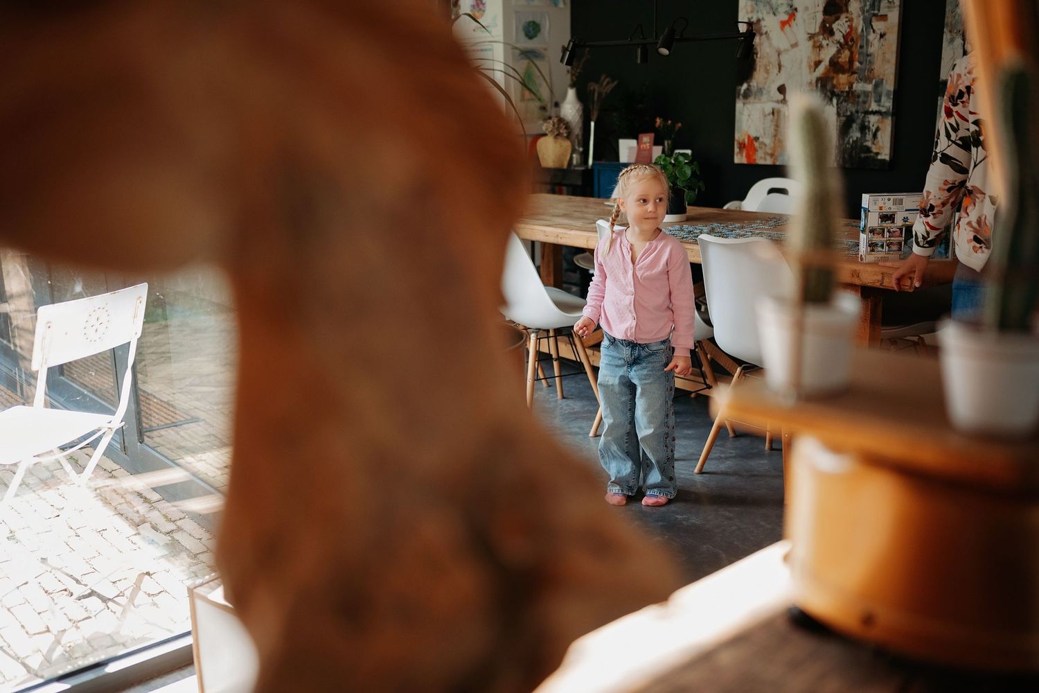 Young child walking through a sunlit modern restaurant interior with white chairs and wooden furniture.