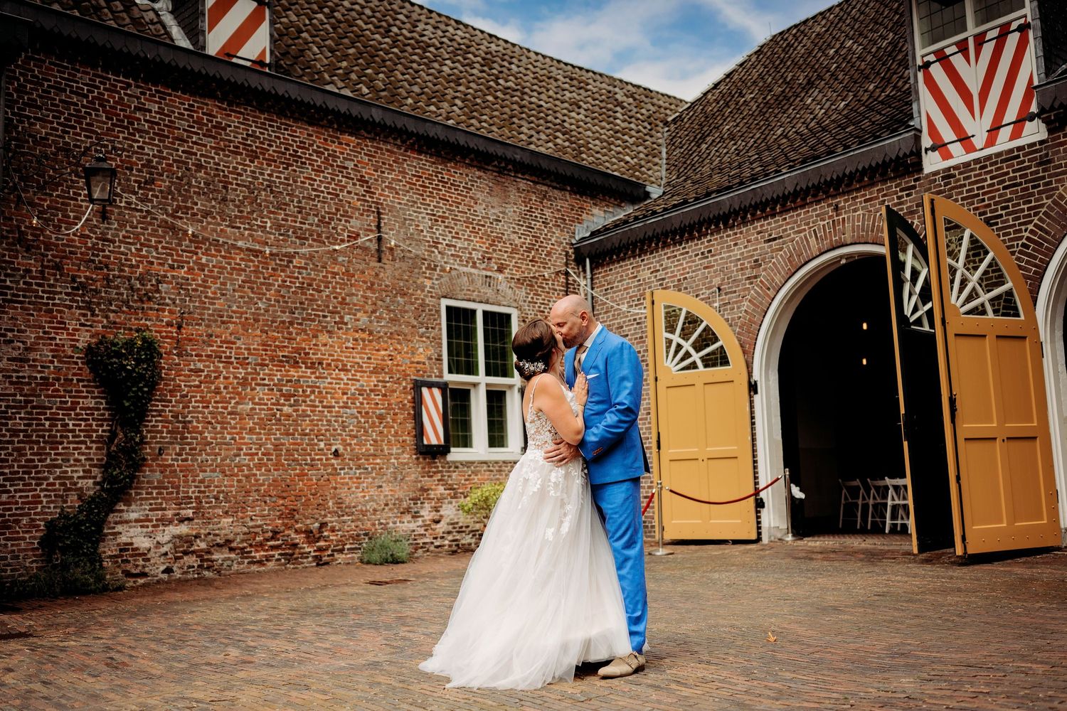 Bride and groom sharing a romantic embrace in a cobblestone courtyard of a rustic brick wedding venue.