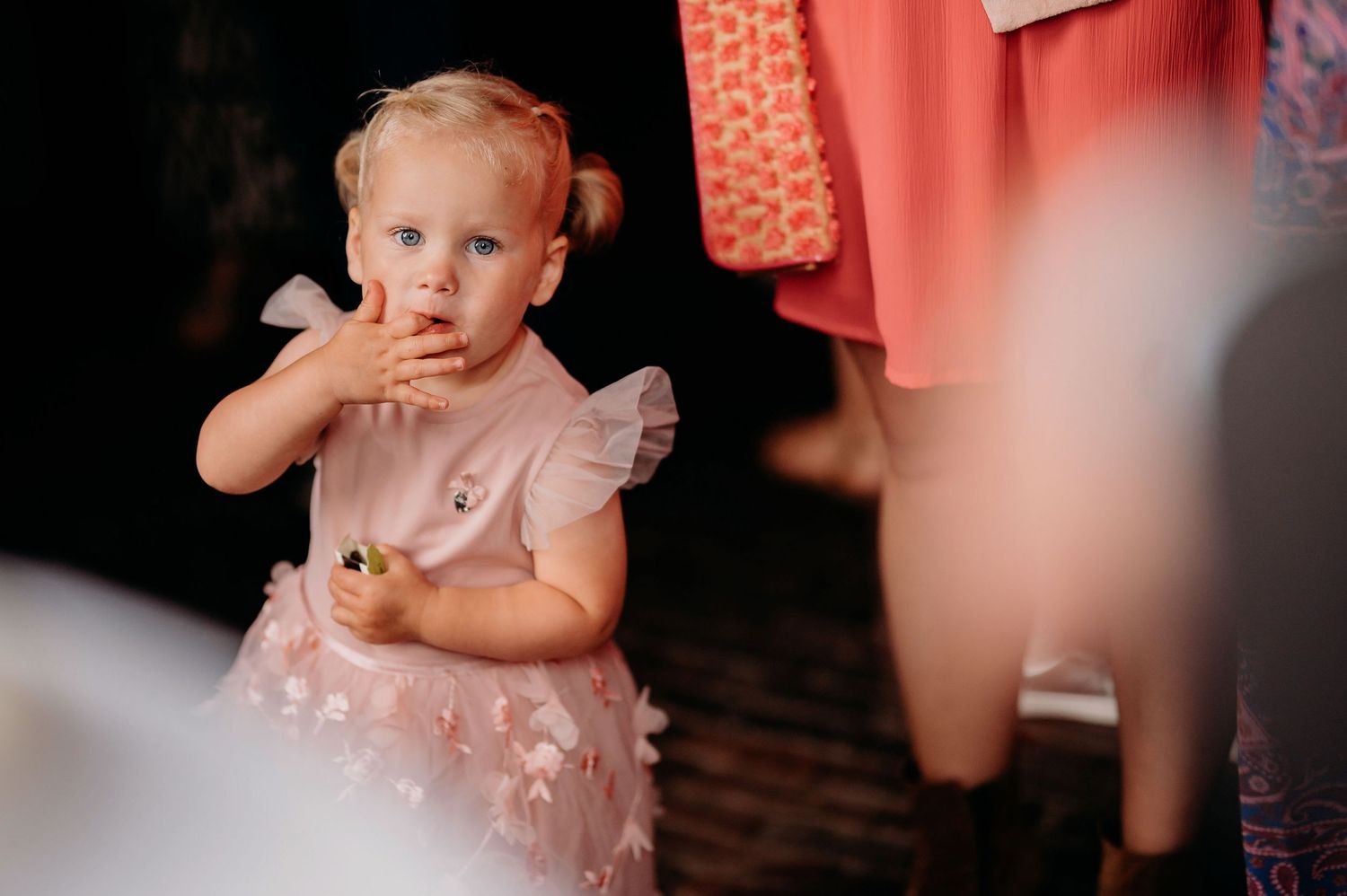 Adorable toddler girl in a pink floral dress with pigtails at a wedding reception.