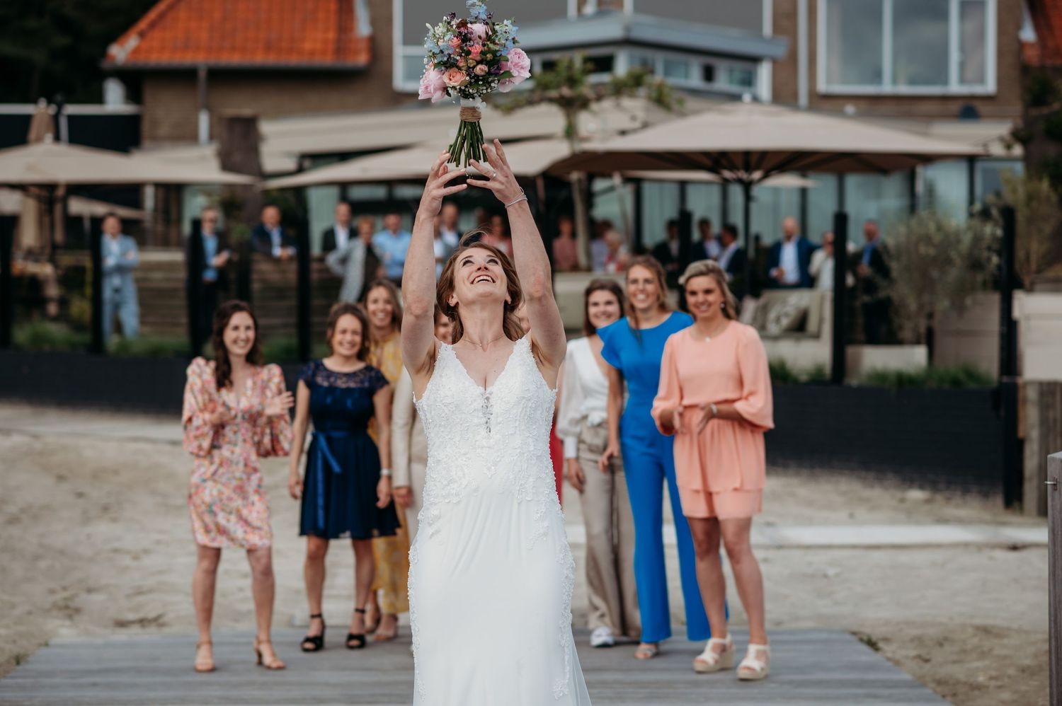 Bruidspaar en gasten lopen over strandpromenade op zonnige dag, bruidsfotografie IJM IJzereman Vught, Brabant.