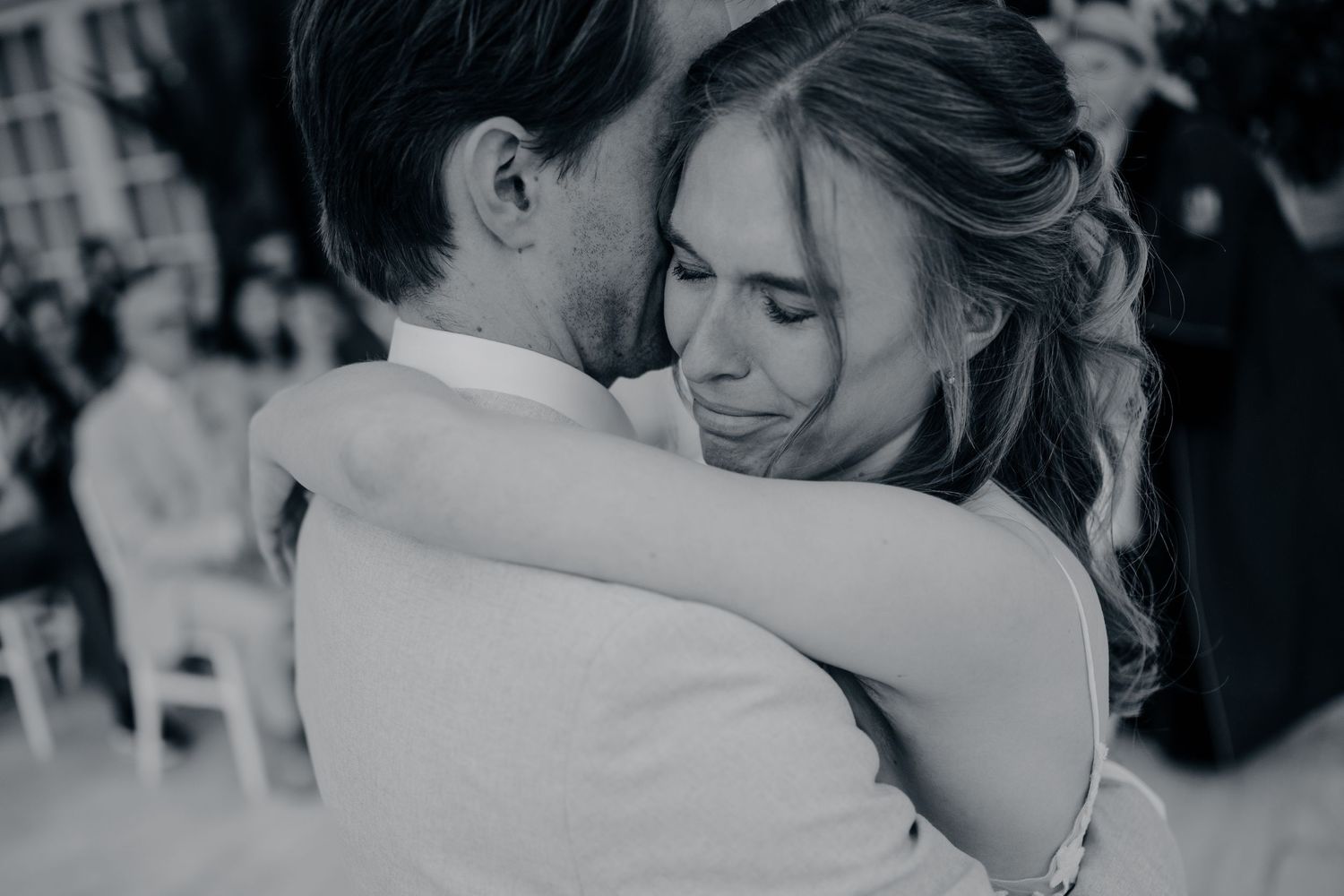 Black and white photo of a bride and groom sharing an emotional first dance embrace at their wedding reception.