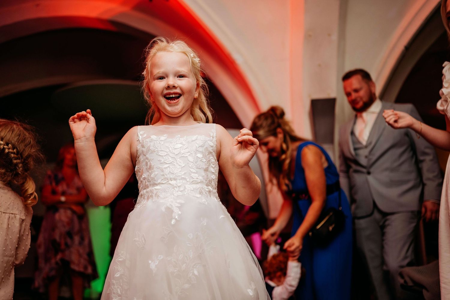 Bruiloftsgasten dansen onder bogen met gekleurd licht, spontane bruidsfotografie en trouwfeest in Den Bosch en Brabant.