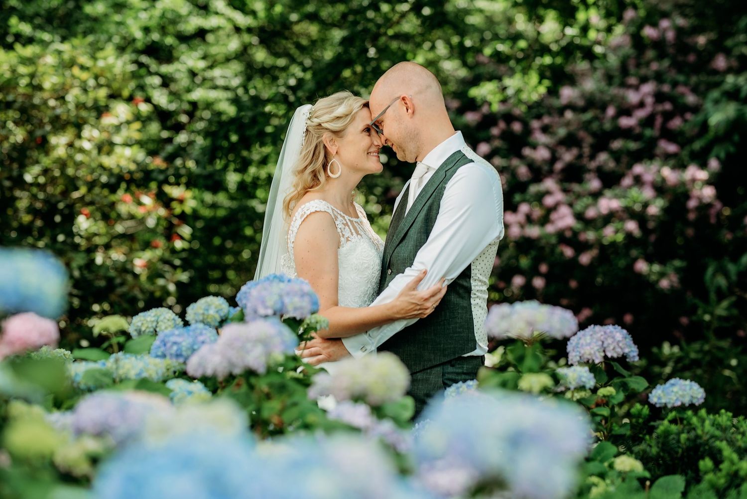 Bruidspaar portret met blauwe hortensia’s op voorgrond, romantische bruidsfotografie Vught, Brabant.