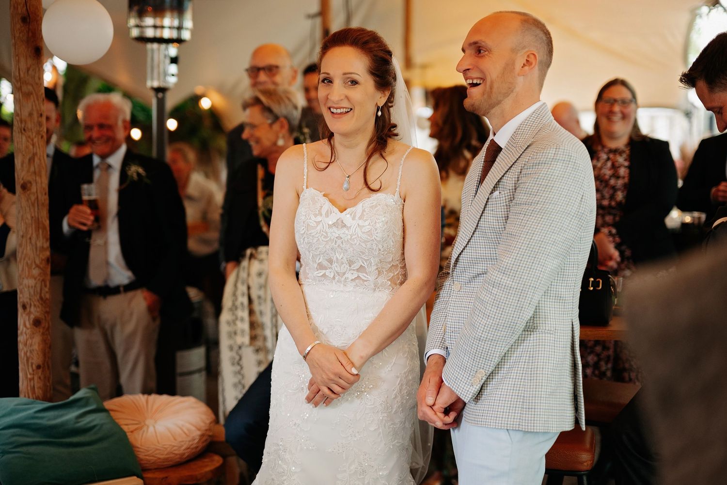 Smiling bride in lace gown and groom in light suit sharing a joyful moment during wedding reception.