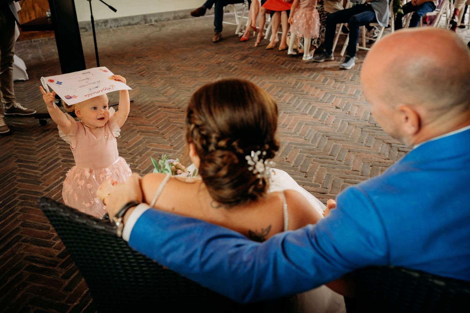 Adorable flower girl holds up drawing for bride and groom during outdoor wedding reception.