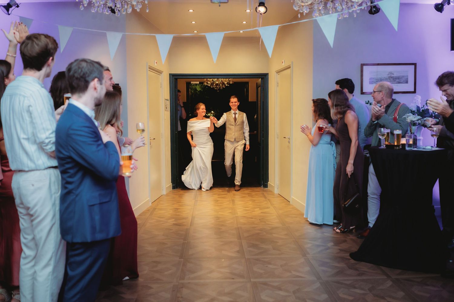 Newlyweds make a grand entrance into the reception hall as guests line up and applaud on both sides.