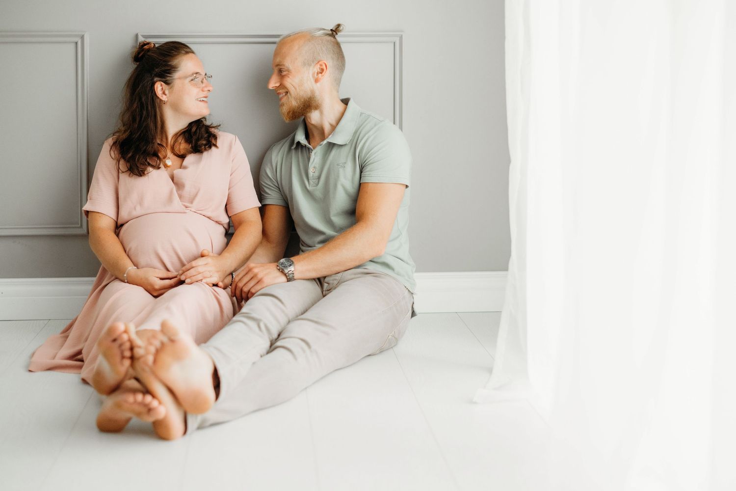 Intieme zwangerschapsfoto van koppel zittend samen op witte vloer, zwangerschapsfotografie Brabant
