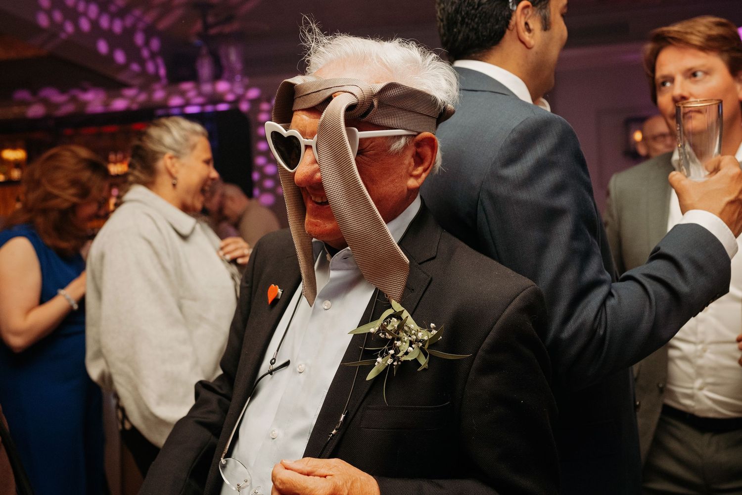Elderly wedding guest wearing novelty oversized sunglasses and hat dancing at reception.