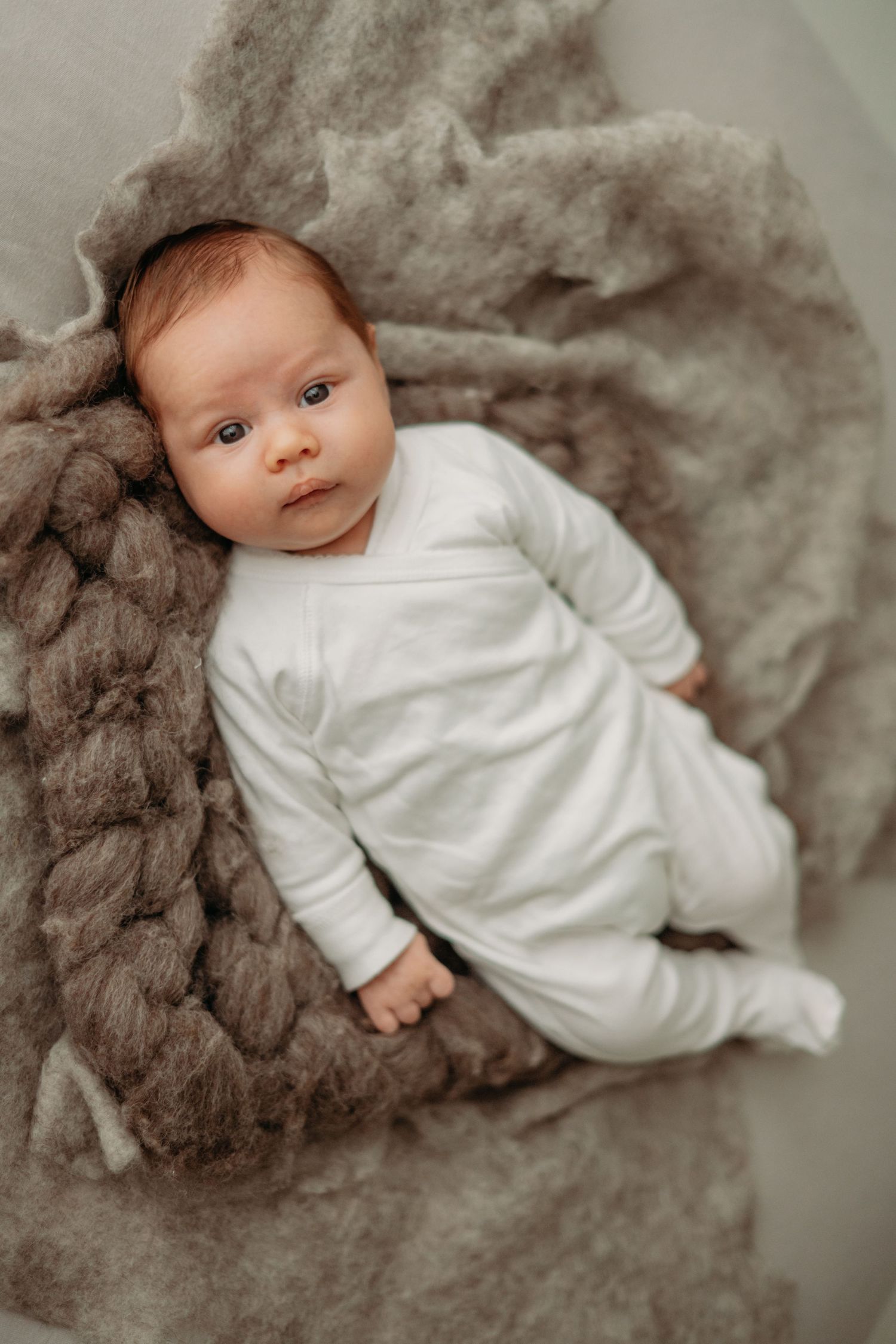 Pasgeborene in witte onesie liggend op zachte grijze deken in studio, newbornfotografie Brabant