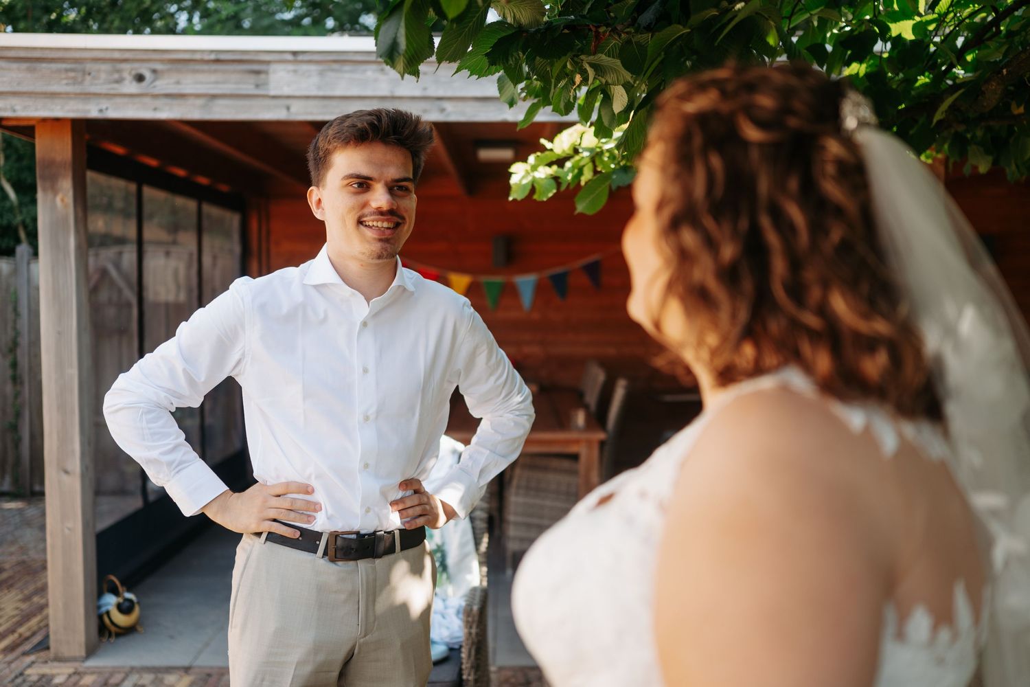 Smiling groom in white shirt admires bride in wedding dress during outdoor ceremony.