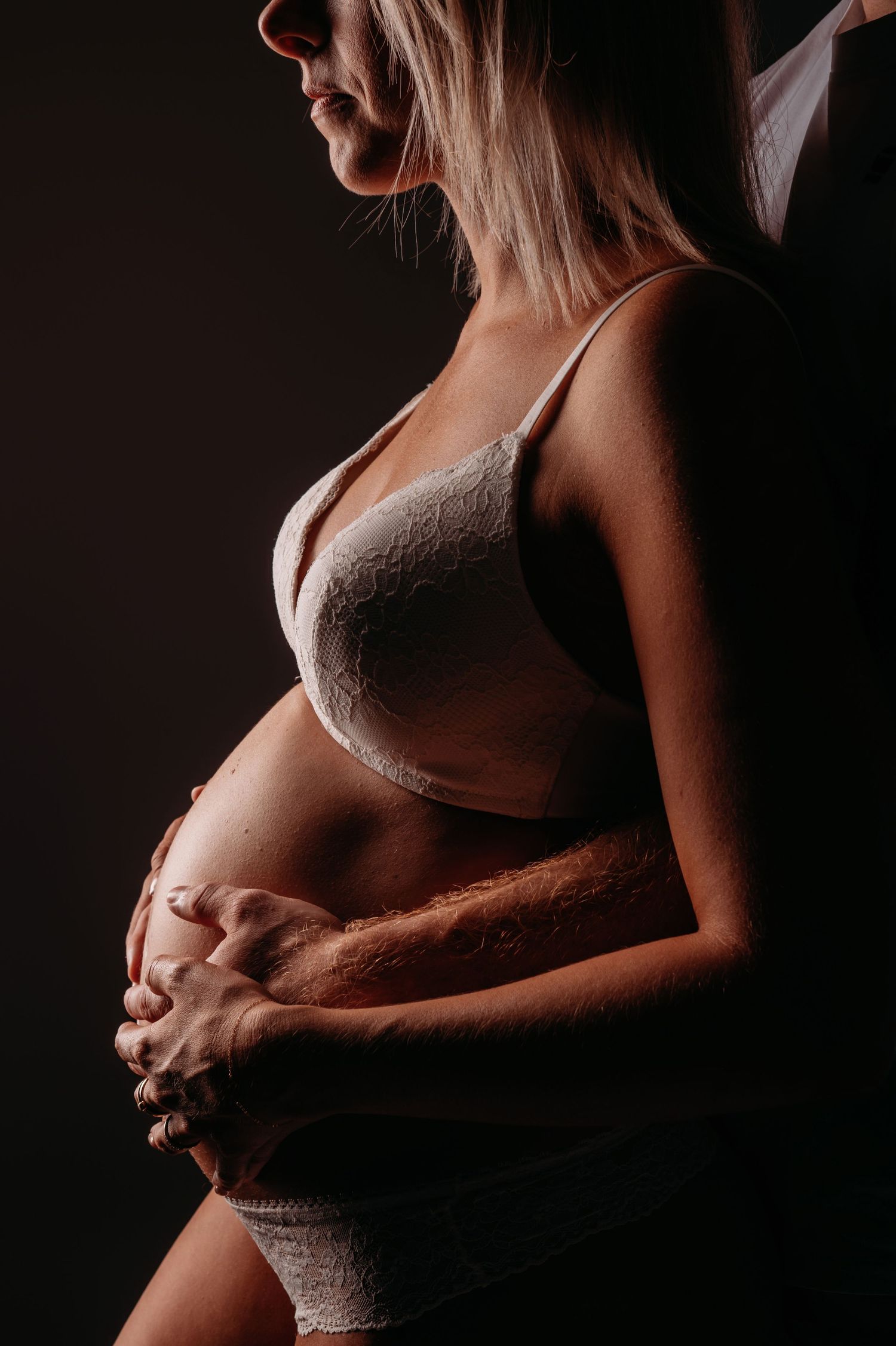 Artistiek silhouet van zwangere vrouw in lingerie tegen donkere achtergrond, zwangerschapsfotografie Brabant