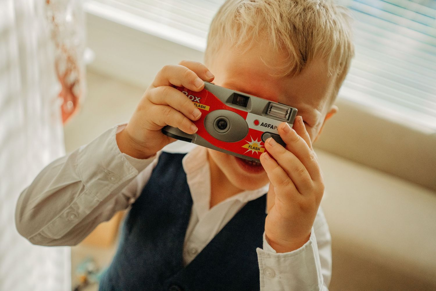 Kind met rood vintage camera maakt foto bij raam, sfeervolle bruidsfotografie bij Boscafé Oisterwijk, Brabant.