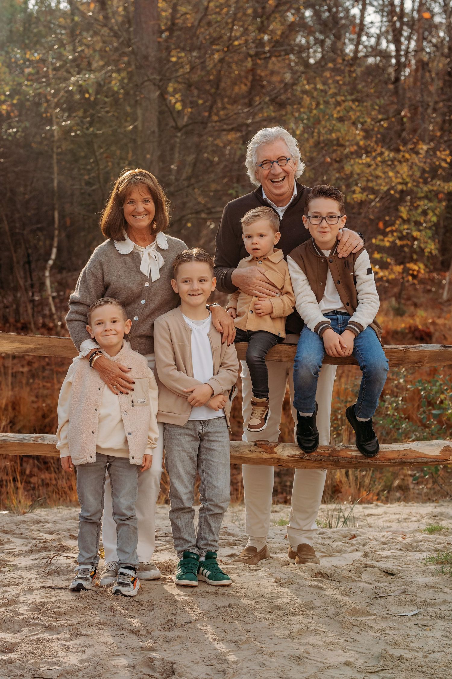 Uitgebreide familiegroep casual zittend op houten bank tijdens herfstshoot, familieshoot Brabant