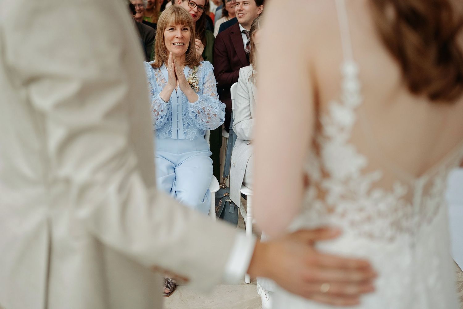 Emotional wedding guest in blue claps with joy as bride and groom stand at altar during outdoor ceremony.